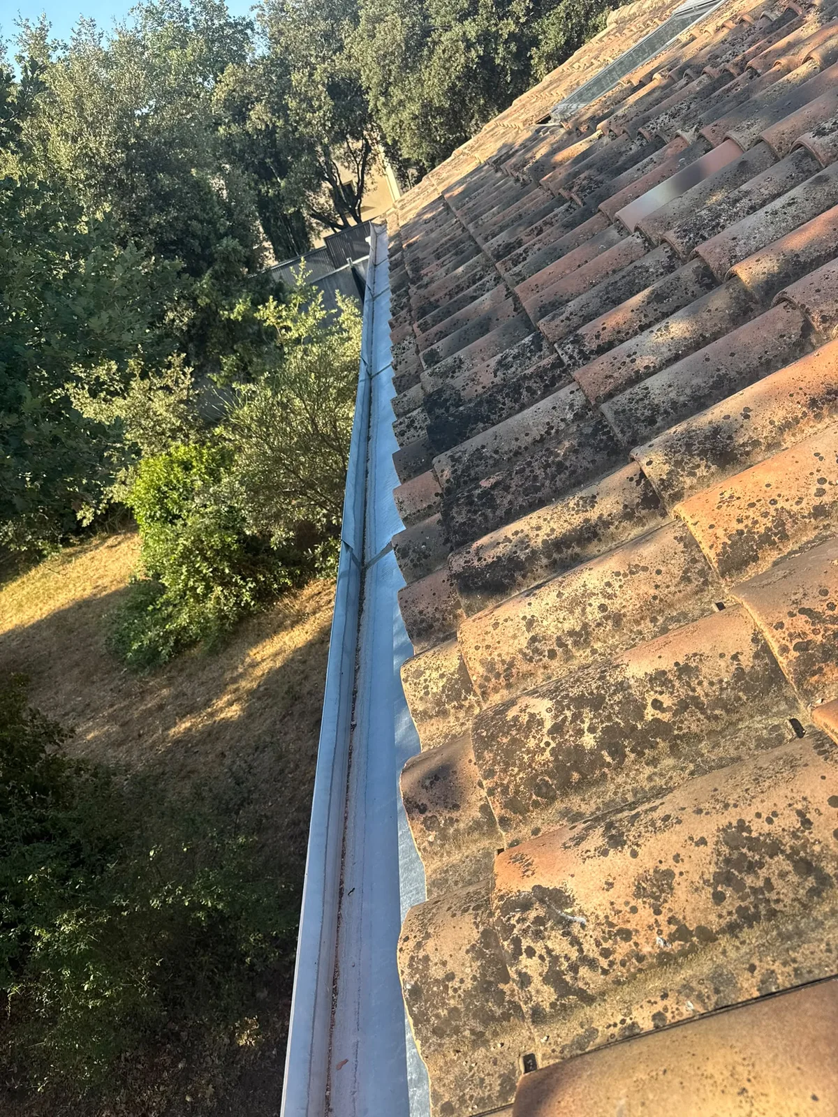 Gouttière métallique le long d’une couverture en tuiles patinées
